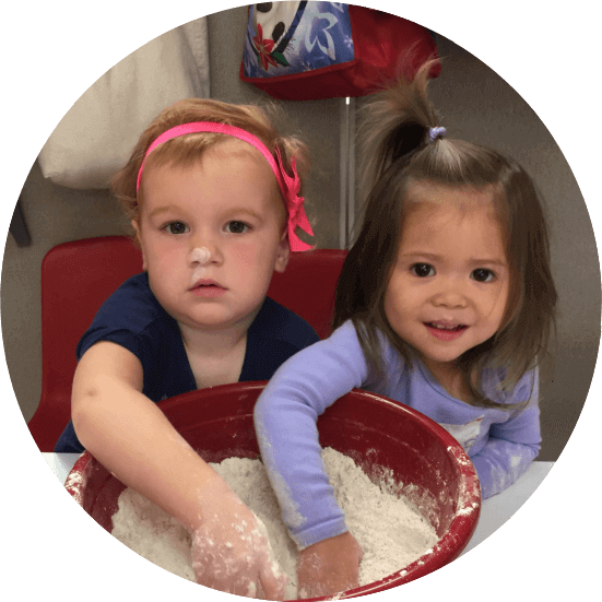 Two toddlers playing with flour in a mixing bowl during a sensory activity