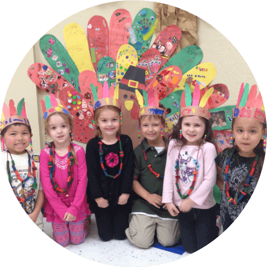 Preschoolers in handmade headdresses in front of a colorful turkey art project